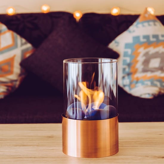 Photo d'un photophore au bio-ethanol posé sur une table en bois, dans un salon.